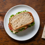 Déjeuner simple vu de dessus sur une table de bistrot en bois : sandwich sur une assiette blanche, verre d'eau et serviette en papier