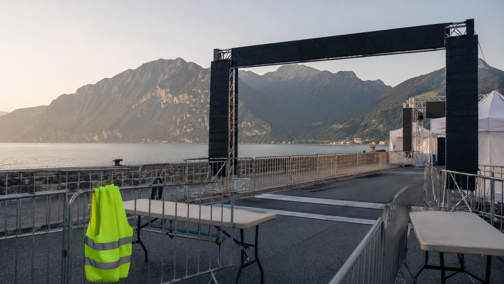 Une zone d'arrivée en cours d'installation au bord d'un lac : barrières, tables pliantes et un gilet fluo accroché