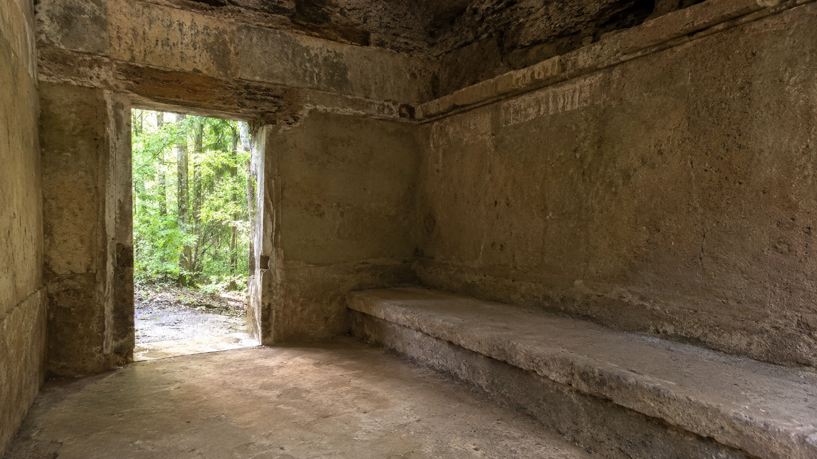 L'intérieur d'une petite chambre de maçonnerie fouillée, murs enduits et banquette de pierre, éclairée par une seule porte