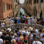 Pont sur un canal venitien bonde d'une foule anonyme de touristes en plein jour, batiments pastel et gondole