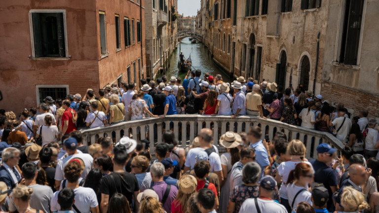 Pont sur un canal venitien bonde d'une foule anonyme de touristes en plein jour, batiments pastel et gondole
