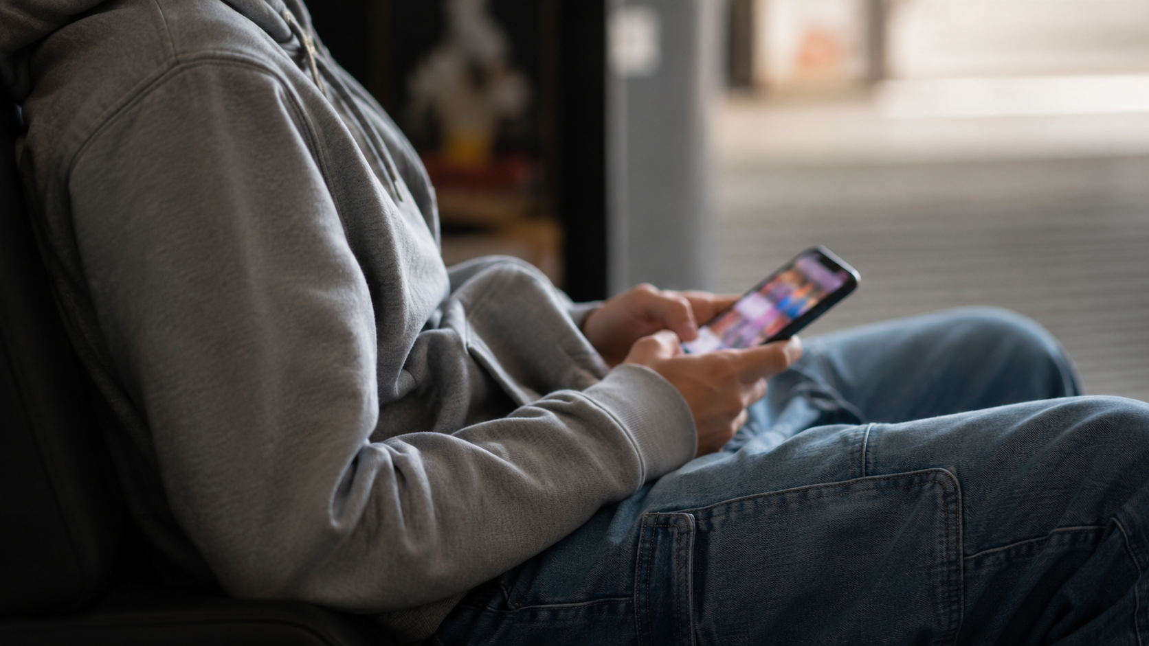 Les mains d'un jeune tenant un smartphone avec une interface de réseau social générique, aucun visage visible