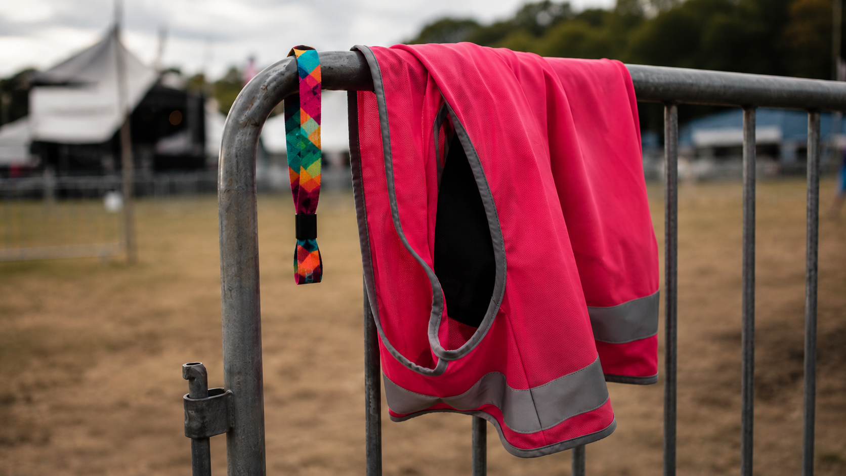 Gros plan sur une chasuble de bénévole colorée et un bracelet en tissu accrochés à une barrière de festival