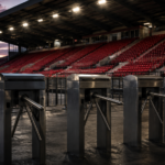 Tribune de stade vide au crépuscule, rangées de sièges rouges et tourniquets fermés au premier plan.