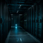 Allée de datacenter la nuit, deux rangées de baies de serveurs constellées de LED d'état, lueur bleu-vert, aucune présence humaine