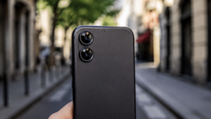Gros plan sur le dos d’un smartphone tenu à la main, deux objectifs alignés reflétant la lumière du jour, rue floue en arrière-plan.