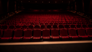 Une salle de cinéma vide photographiée depuis le bord de l’écran, les rangées de fauteuils rouges descendant dans la pénombre.
