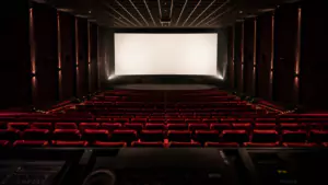 Salle de cinéma vide vue depuis la cabine de projection, fauteuils rouges alignés et écran blanc allumé