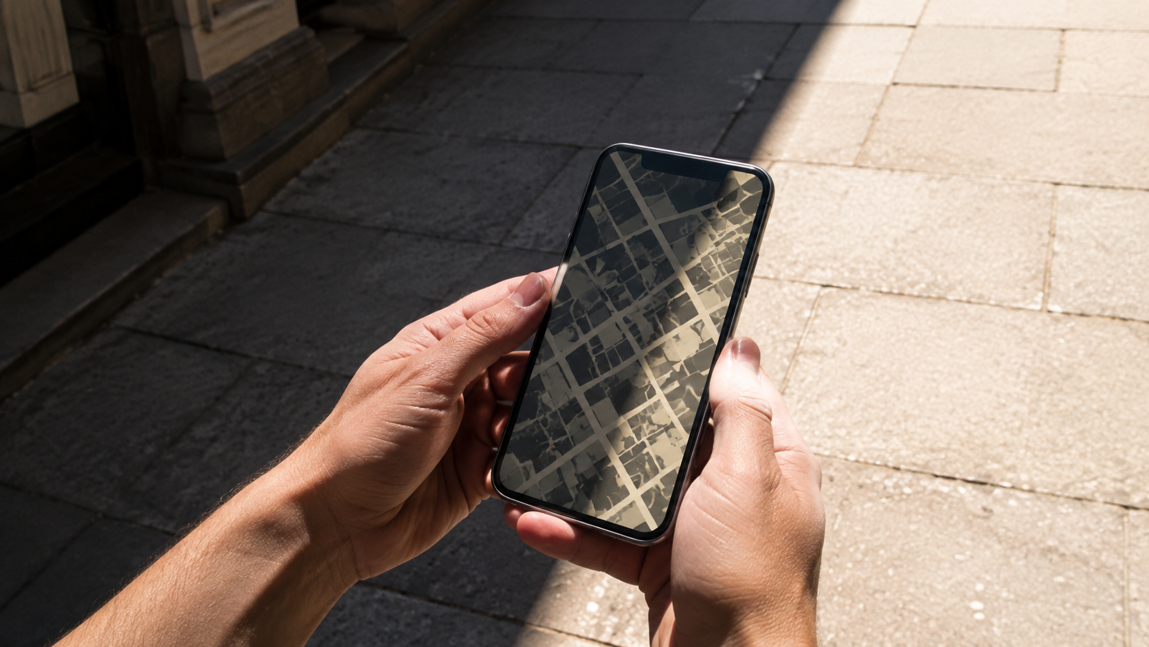 Des mains tiennent un téléphone sur un trottoir ensoleillé, l’écran affiche une carte où des zones sombres se détachent des zones claires.