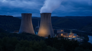 Centrale nucléaire au crépuscule dans une vallée boisée, deux tours de refroidissement et un panache de vapeur blanche.