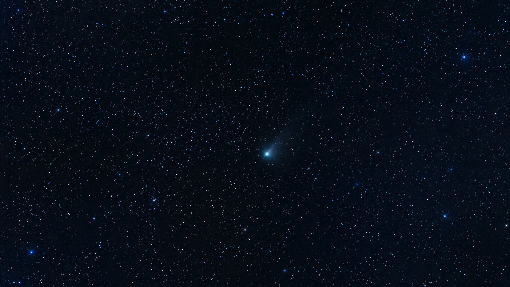 Champ d'étoiles en pose longue avec une petite comète diffuse et sa queue pâle, dominante bleu froid