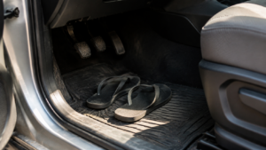 Paire de tongs posée sur le tapis de sol côté conducteur, au pied des pédales d'une voiture