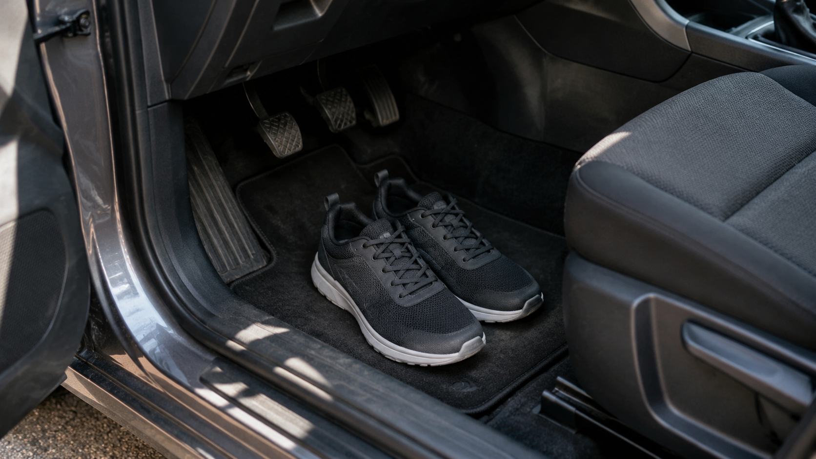 Pédales d'une voiture et paire de baskets fermées posée sur le tapis de sol, prêtes à être enfilées