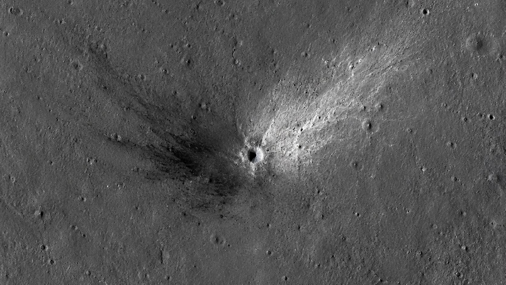 Gros plan orbital d’un petit cratère lunaire, éjectas sombres et clairs formés en V asymétrique sur le régolithe gris