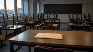 Salle de classe vide au petit matin, chaises retournées sur les tables et enveloppe administrative posée seule sur le bureau, sans personne visible