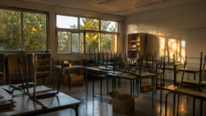 Salle de classe vidée en fin d'année scolaire, chaises empilées sur les tables et cartons au sol.