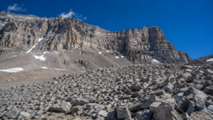 Champ de blocs rocheux gris et anguleux s’étalant au pied d’une paroi raide de haute montagne dans l’Ouest américain, ciel bleu profond