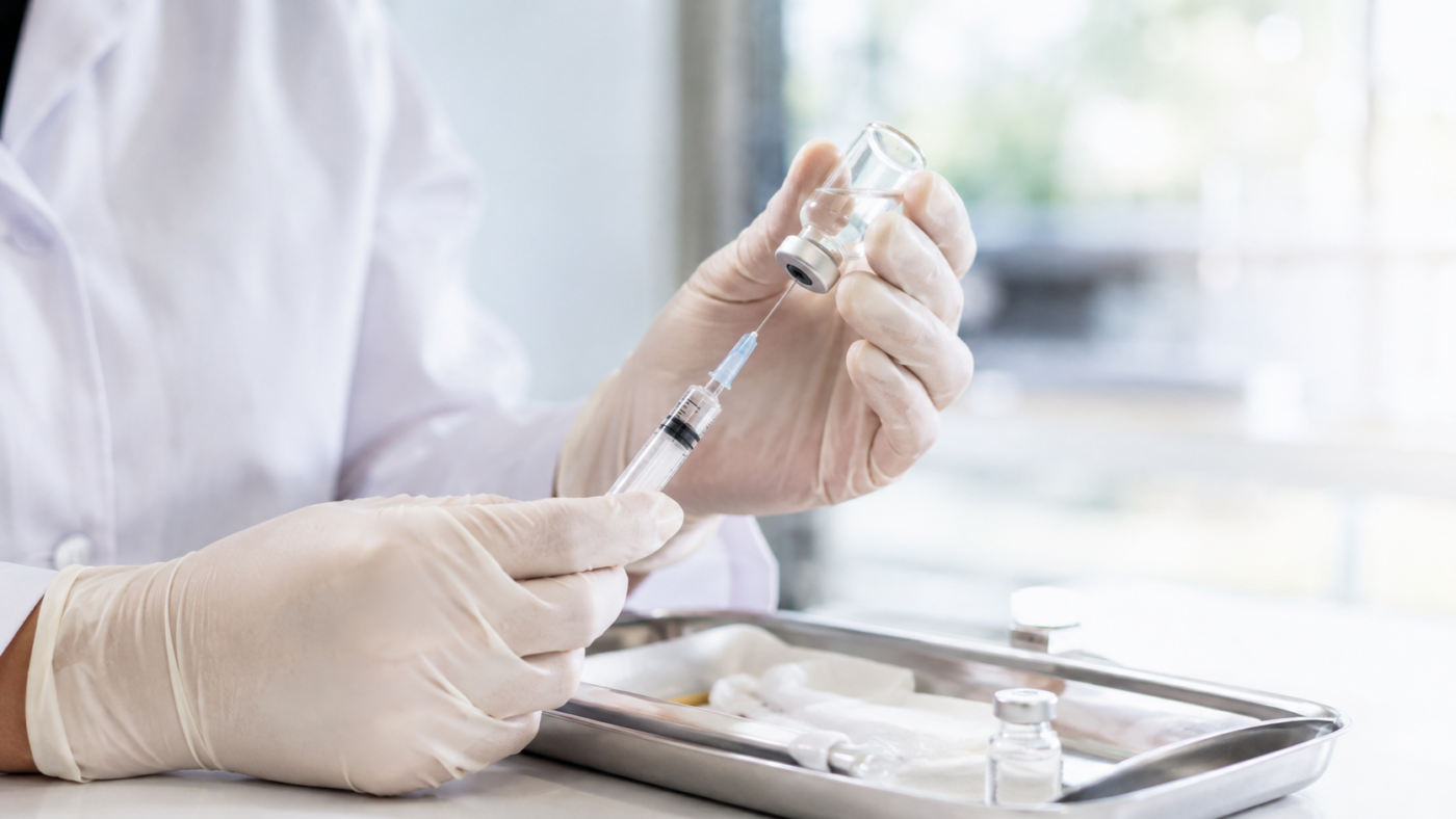 Gros plan sur les mains gantées d'une soignante préparant une seringue de vaccin sur un plateau, dans un cabinet médical lumineux, sans visage reconnaissable.