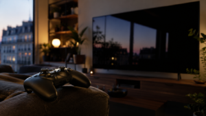 Manette de jeu posée sur l’accoudoir d’un canapé dans un salon au crépuscule, grand écran éteint reflétant la fenêtre