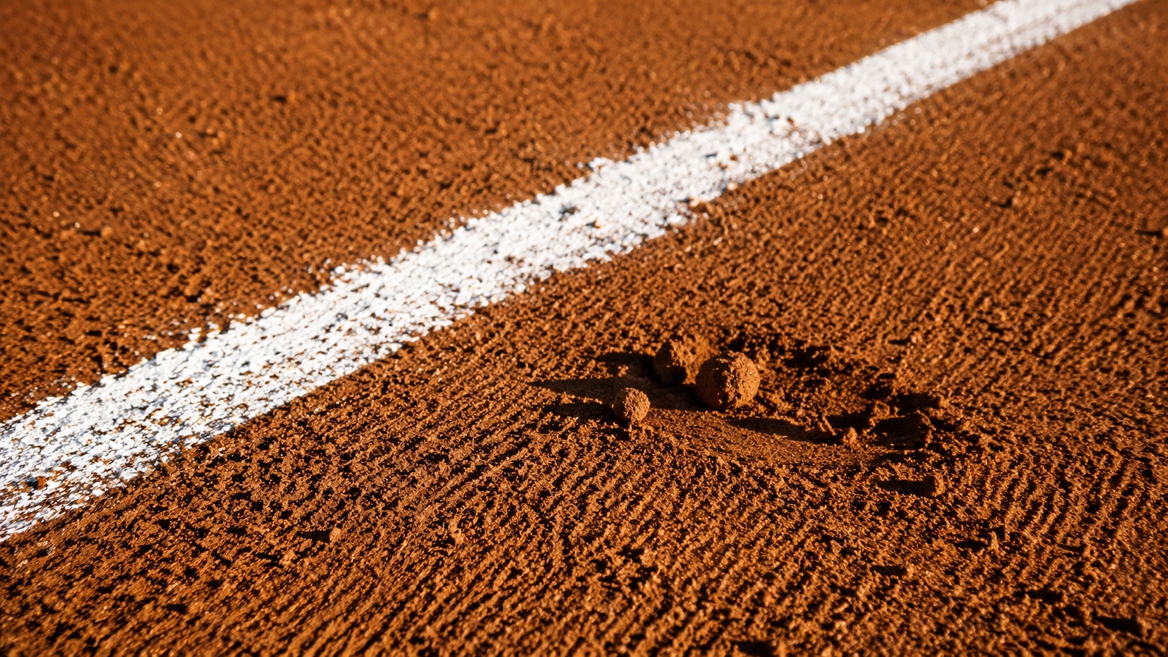 Gros plan sur la terre battue fraîchement ratissée d'un terrain de baseball au soleil, avec une ligne blanche tracée à la craie