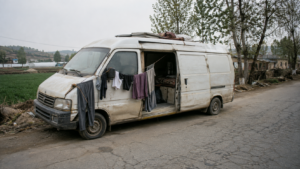 Vieux fourgon blanc cabossé et défraîchi, aménagé pour y vivre, garé sur le bas-côté d’une route de campagne du Shandong, du linge séchant à un fil tendu au rétroviseur, personne dans le cadre