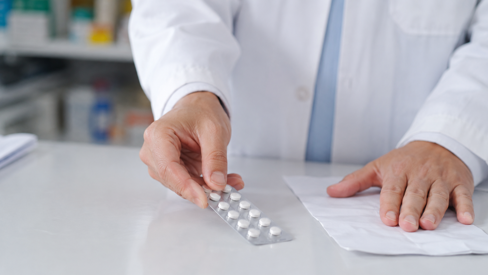 Mains d'un pharmacien poussant une plaquette de comprimés sur le comptoir, à côté d'une ordonnance.