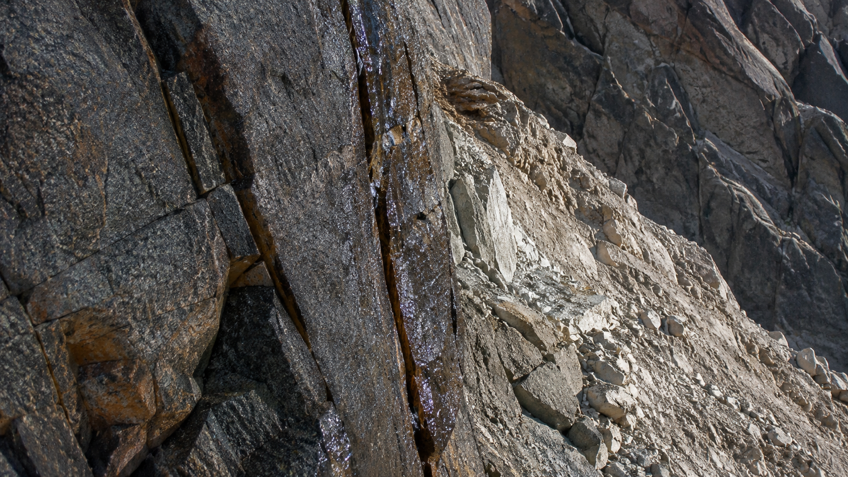 Paroi de granit d’altitude en fin d’été, fissures suintantes vidées de leur glace, blocs anguleux instables et cicatrice claire d’un éboulement récent.
