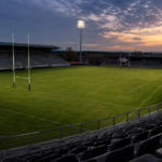 Stade de rugby vide vu des tribunes au crépuscule, pelouse nue et poteaux, sans public