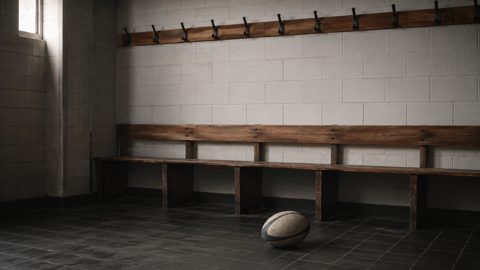 Vestiaire de rugby vide, banc en bois et patères nues, un ballon posé au sol
