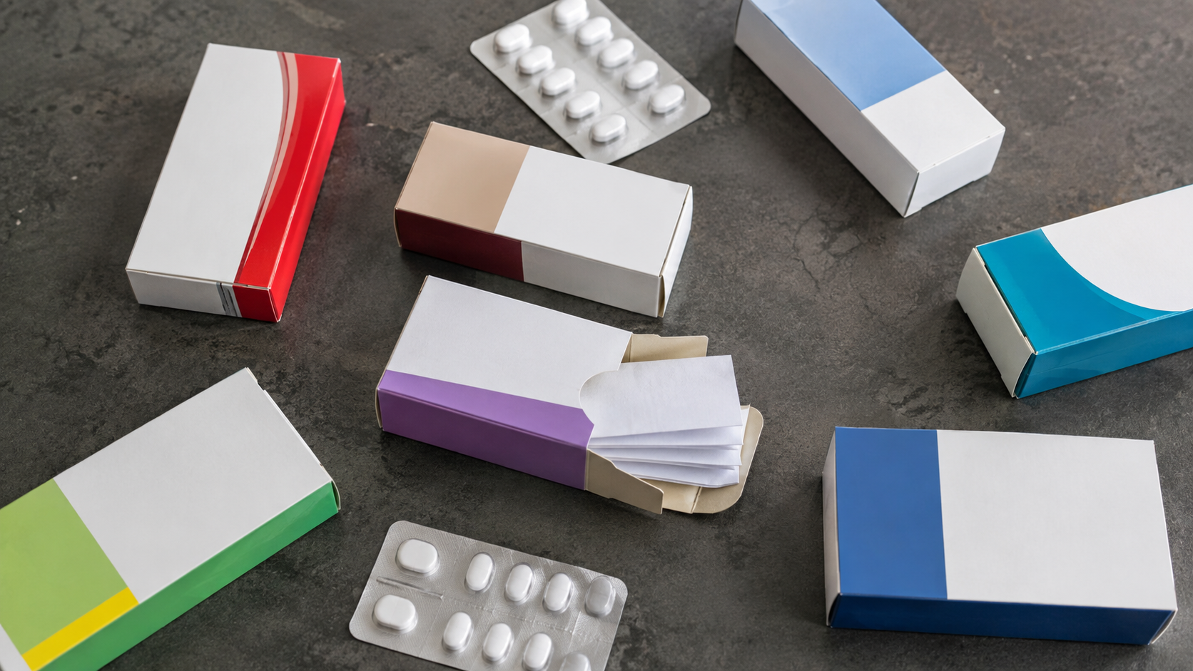 Vue de dessus de sept boîtes de médicaments sans marque et de plaquettes de comprimés disposées sur un plan de travail gris.