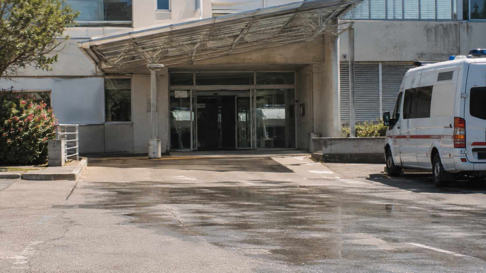 Salle d'attente hospitalière en été, fontaine à eau au premier plan et silhouettes floues de dos, aucun visage reconnaissable.