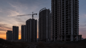 Tours résidentielles inachevées au crépuscule, façades de béton nu et grue immobile.
