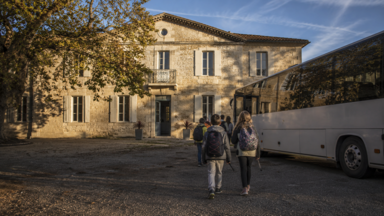 La Bastide de Madame à Couffoulens, école provisoire pour les enfants de Pomas, un bus scolaire garé devant le bâtiment en pierre au petit matin.