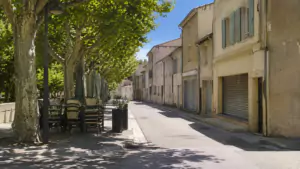 Rue de village française déserte à midi en août, rideaux de fer baissés sur les commerces et terrasse de café repliée sous les platanes