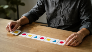 Mains d’un adulte alignant des cartes portant des suites de nombres sur une table en bois clair, lors d’un test de logique.