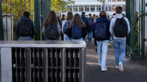 Lycéens vus de dos franchissant la grille d’un lycée français, casiers métalliques à téléphones au premier plan