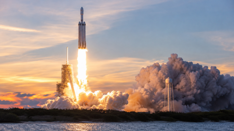 Fusée Falcon Heavy au décollage depuis un pas de tir en Floride, à l'aube, panache de fumée blanche.