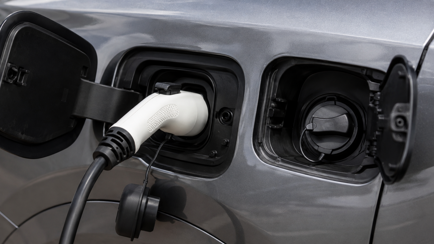 Gros plan sur une prise de recharge branchée à une voiture sans marque visible, la trappe à carburant ouverte juste à côté.