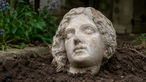 Tête de femme sculptée dans du calcaire clair posée sur la terre fraîchement retournée d’un jardin