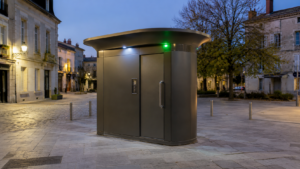 Cabine de toilettes publiques autonettoyantes seule sur une place pavée d’une ville française, à la tombée du jour.