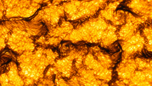 Gros plan sur la surface bouillonnante du Soleil, grains de plasma lumineux séparés de sillons sombres le long desquels s'enroulent de petits tourbillons.