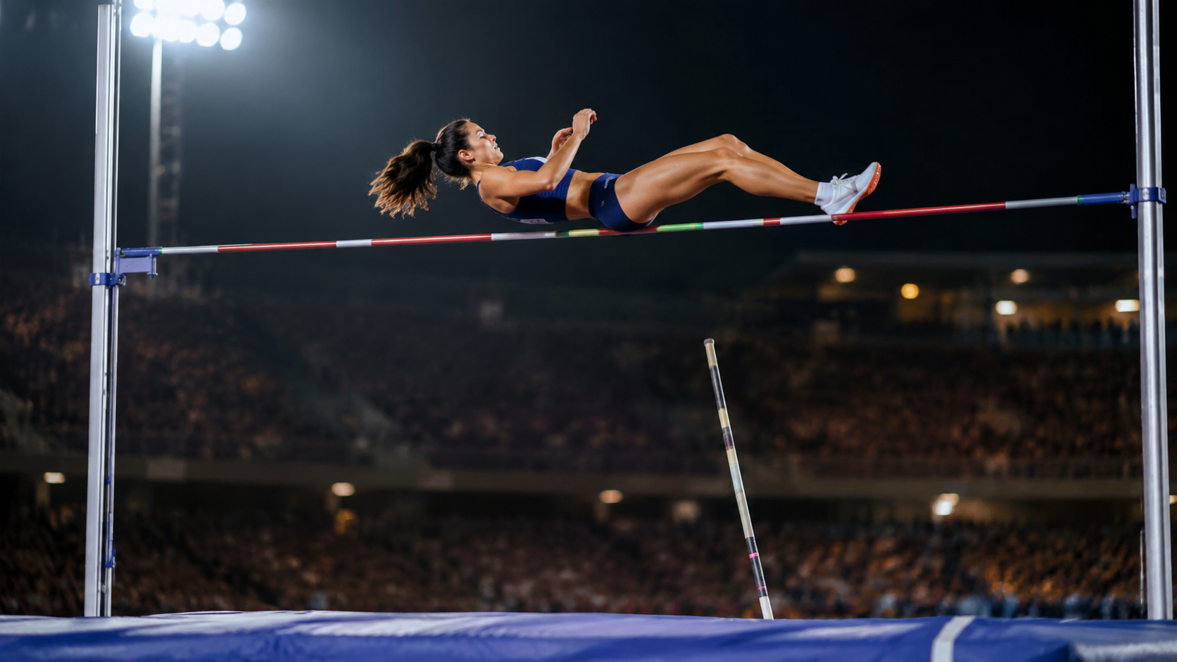 Une perchiste franchit la barre au-dessus du tapis de réception, dans un stade d'athlétisme éclairé de nuit, tribunes floues en arrière-plan.