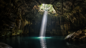 Cénote de jungle aux parois calcaires, eau sombre et immobile éclairée par un unique puits de lumière tombant du plafond