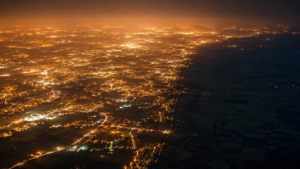 Vue aérienne nocturne d’une plaine européenne couverte d’éclairages orangés continus, avec une mince bande de campagne sombre au bord du cadre.