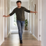 Un adulte debout talon contre pointe dans un couloir clair, yeux fermés, bras légèrement écartés pour tenir l'équilibre.