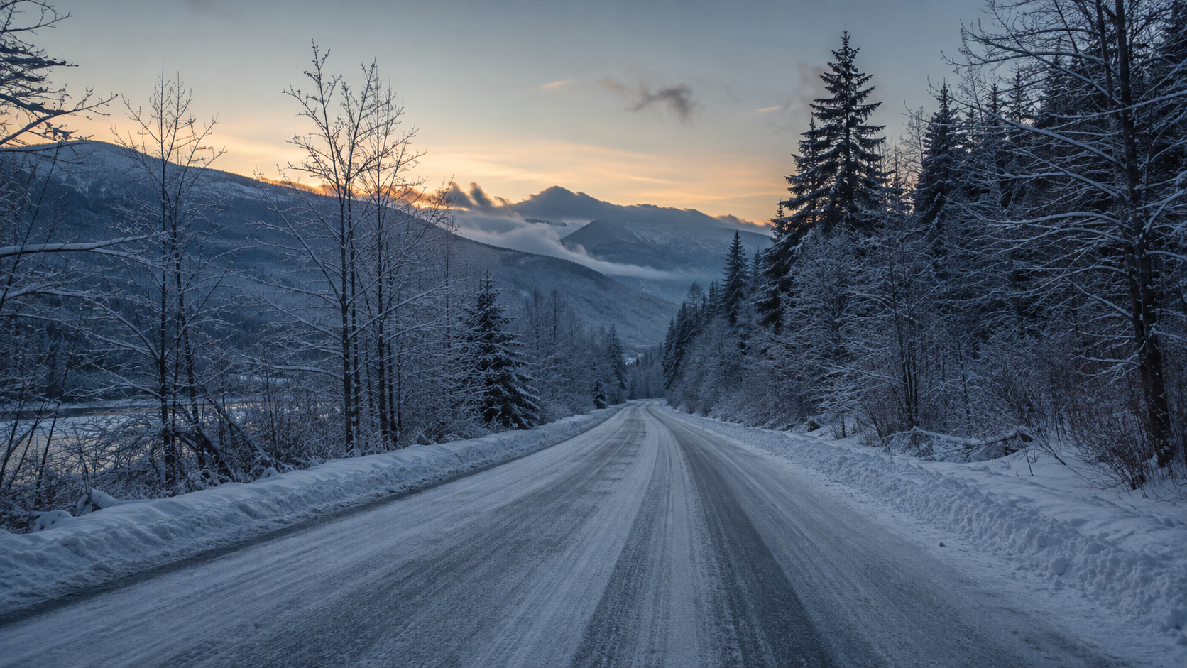 Une route de campagne enneigée du nord-ouest des États-Unis à l’aube, bordée d’arbres nus et de conifères sombres.