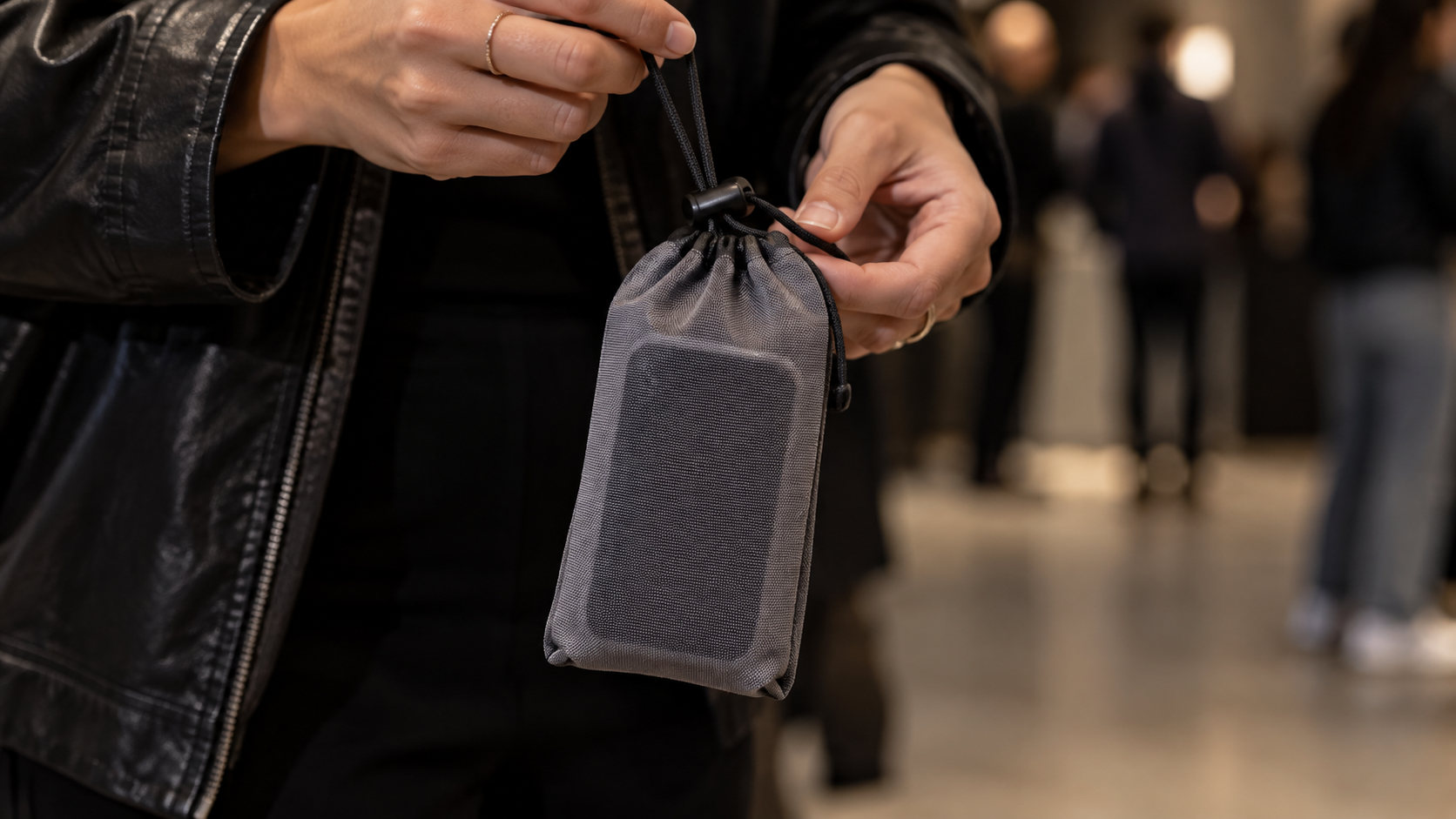 Deux mains tiennent une petite pochette en tissu fermée, suspendue à un cordon, avec un téléphone à l’intérieur.