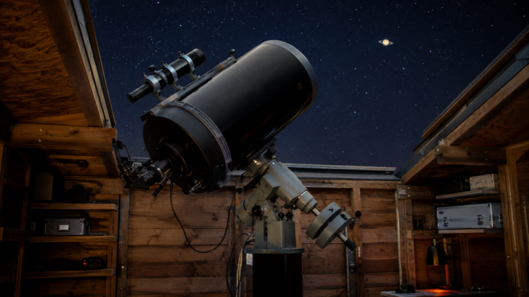 Grand télescope d’amateur sur monture équatoriale, dans un abri de jardin au toit ouvert, pointé vers un ciel étoilé.