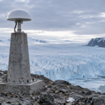 Antenne GNSS blanche sur un pilier de béton ancré dans la roche nue, en bordure d'une calotte glaciaire