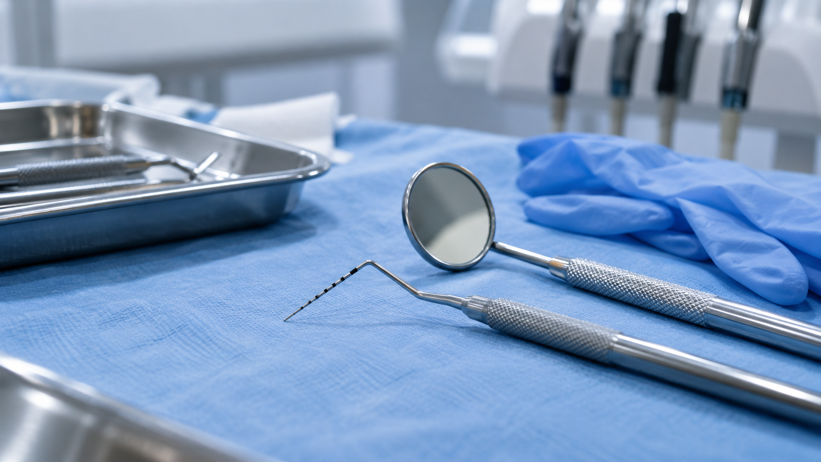 Une sonde parodontale graduée et un miroir dentaire posés sur un champ bleu, à côté de gants d’examen.